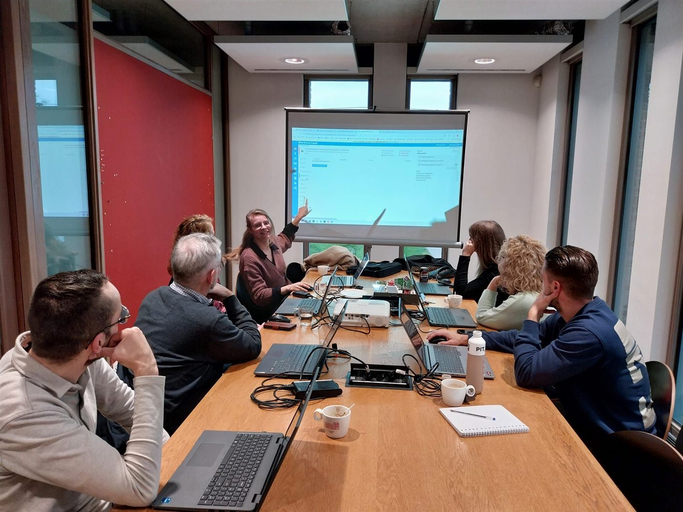Marije geeft een training aan een team rond een tafel met laptops